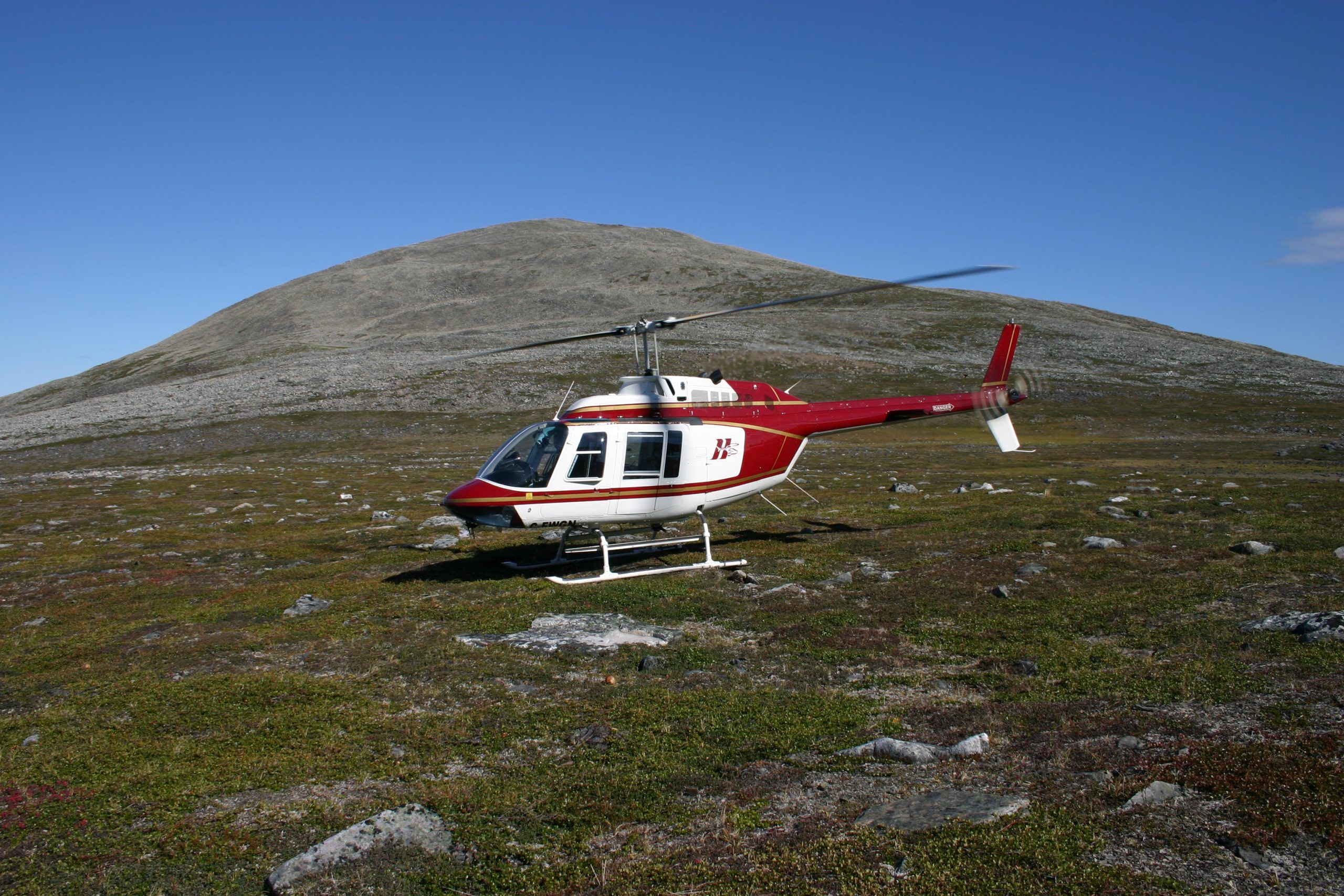HTS Bell 206B parked on open tundra below a rounded hill
