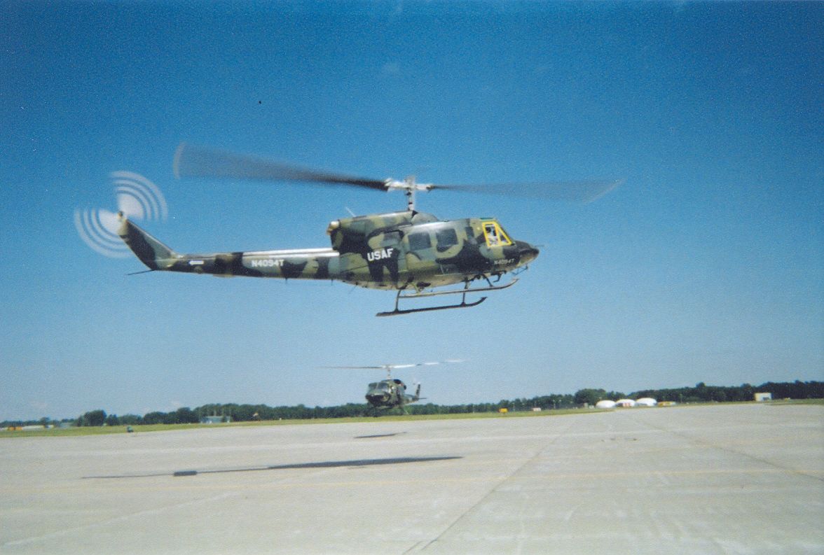 Camouflaged utility helicopter flying low over a runway