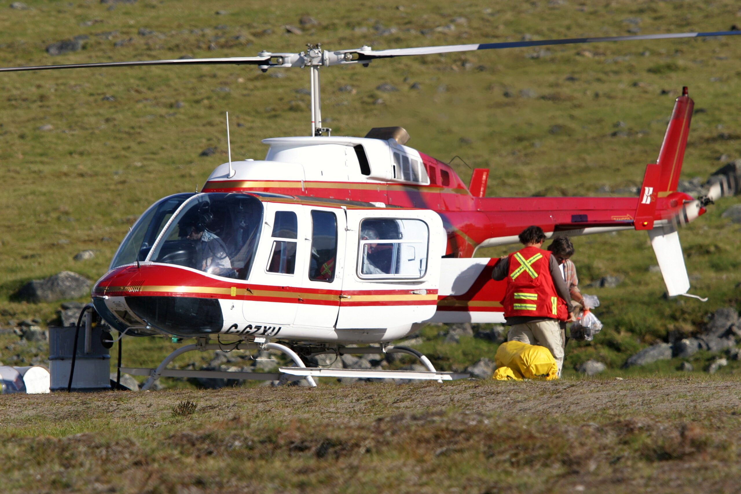 Bell 206L on the ground at a remote work site, a crew member in hi-vis beside it