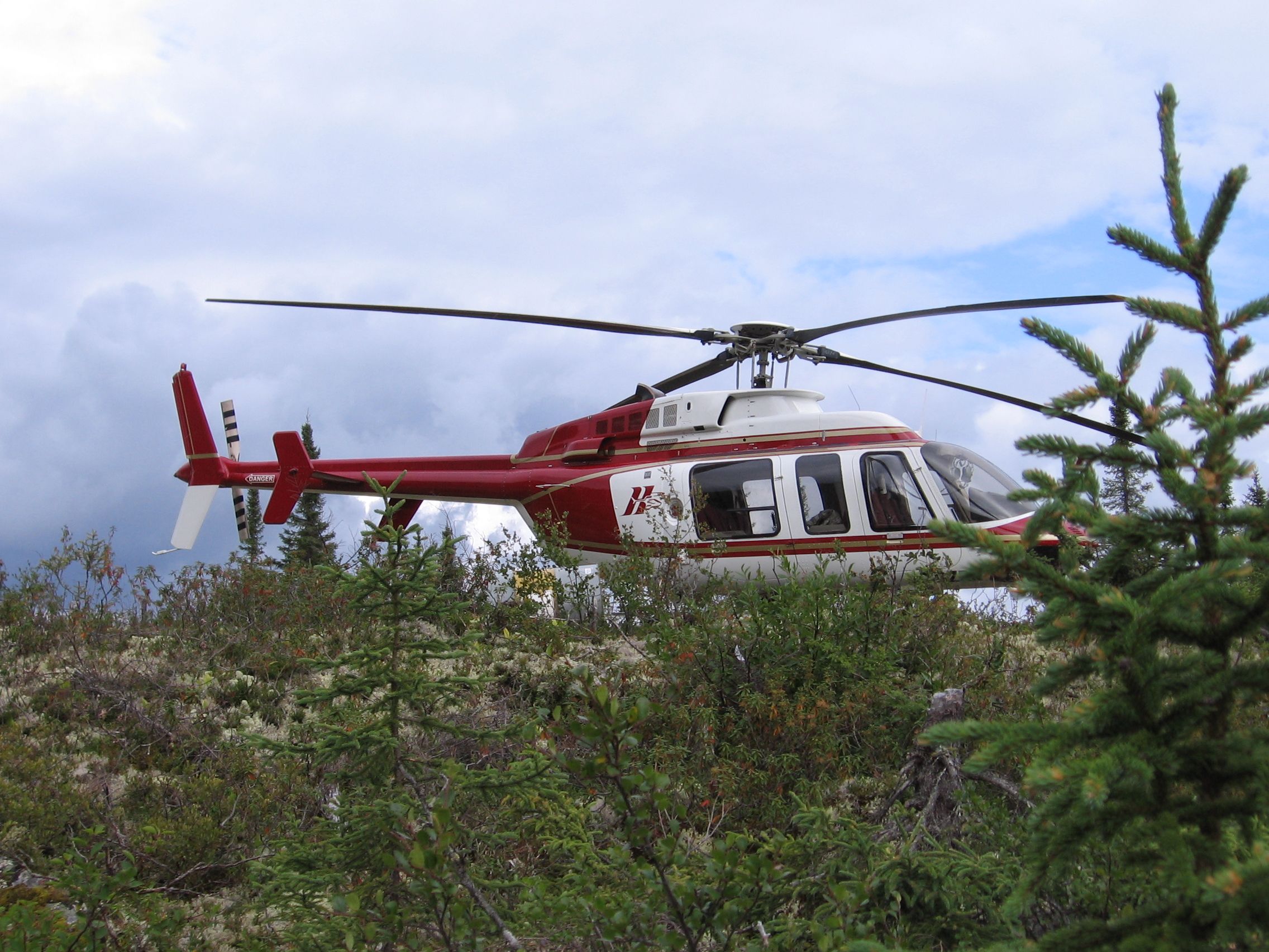 HTS Bell 407 landing among spruce trees at a remote site