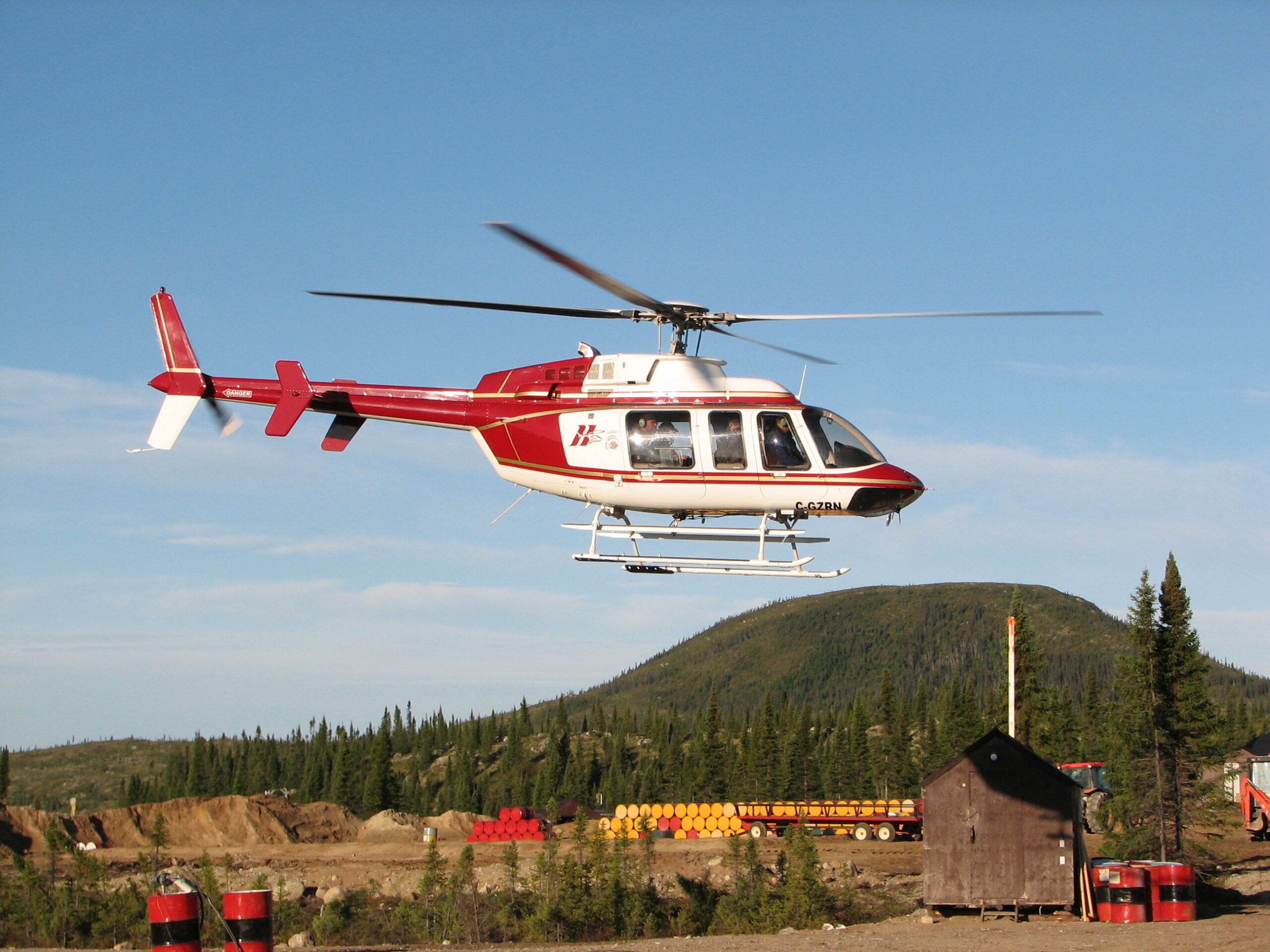 HTS Bell 407 in red and white livery flying low over a bush camp
