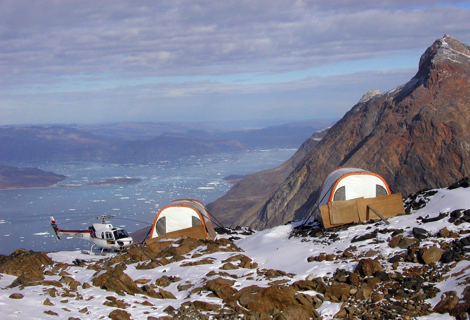 HTS helicopter parked beside dome tents at a mountain camp above an icy bay
