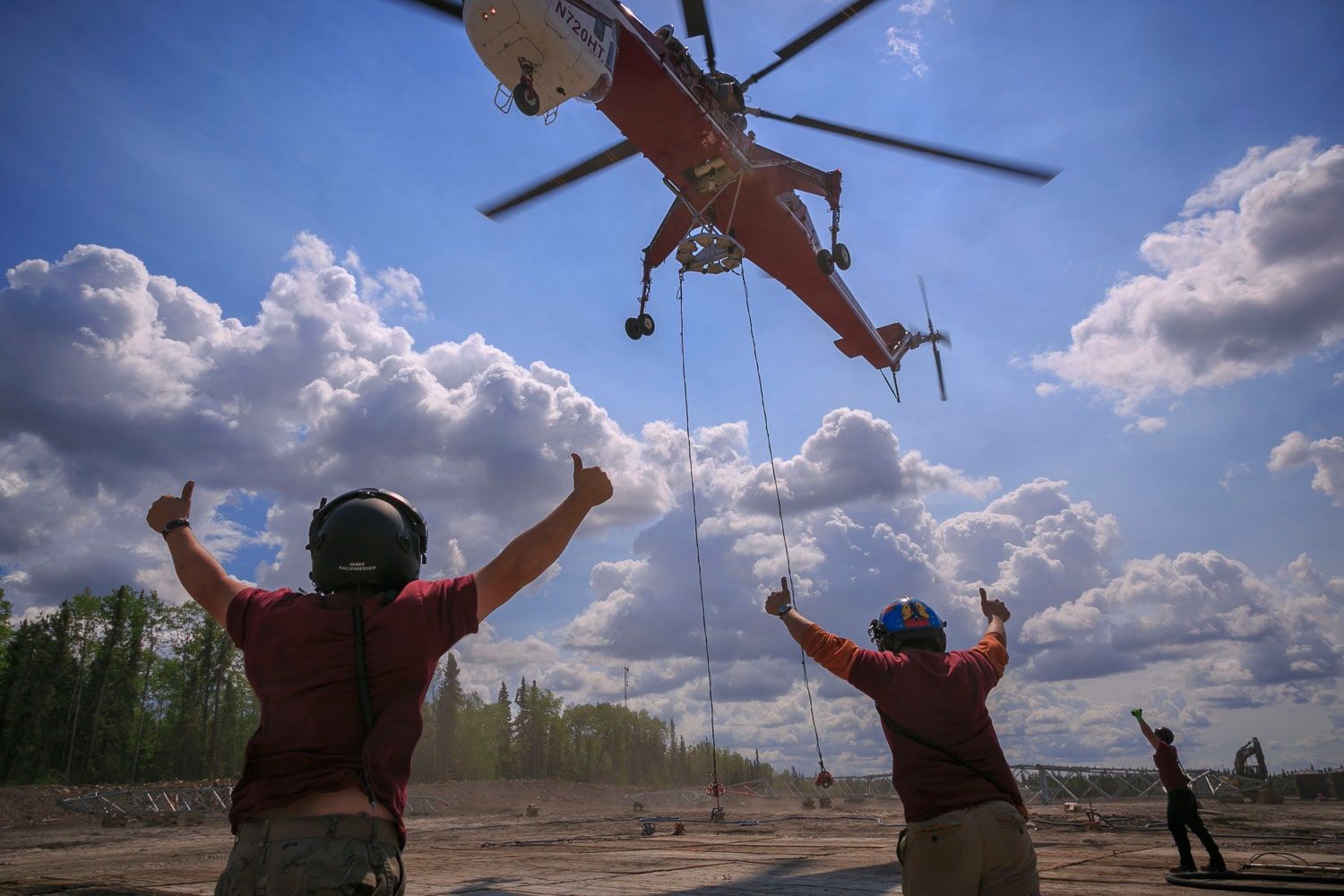 Two ground crew with arms raised, signalling a Skycrane overhead on a long line