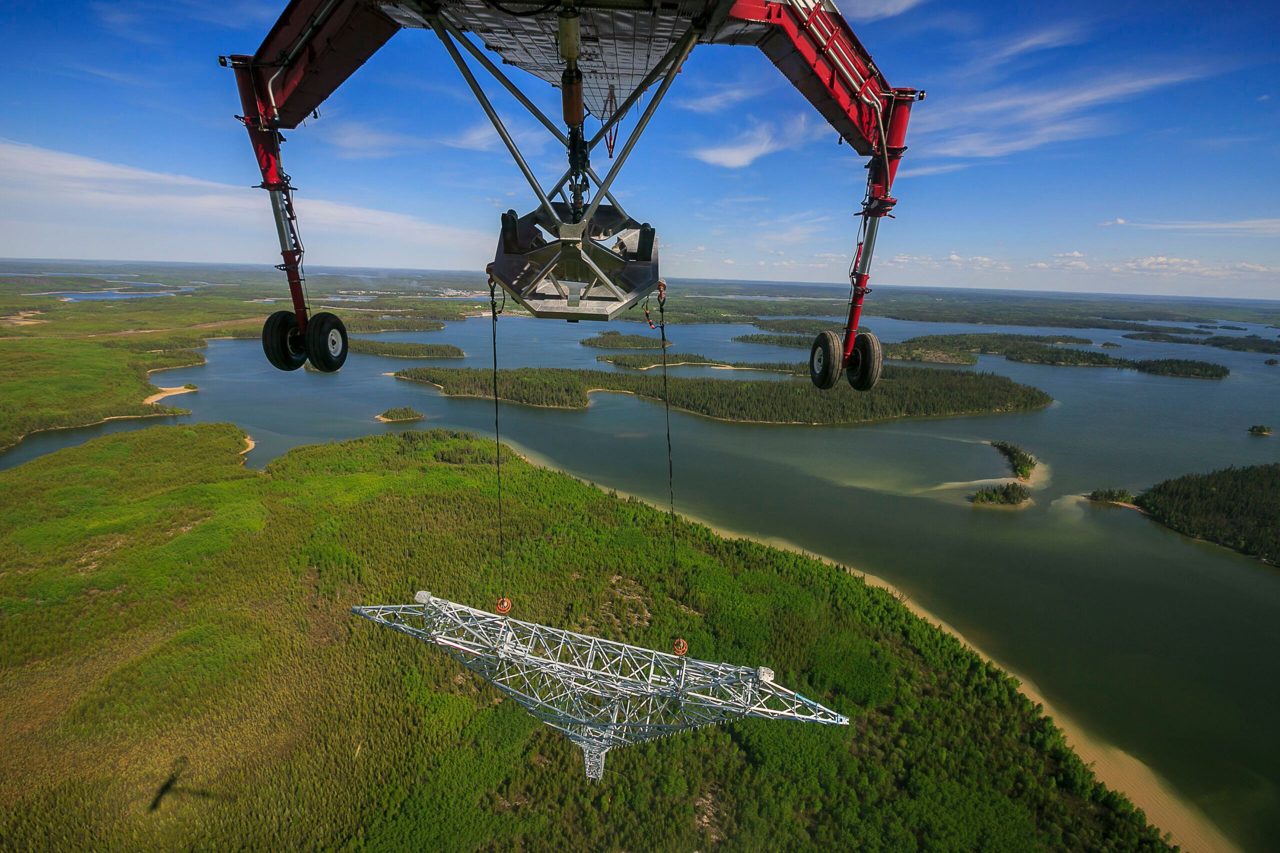 View from beneath a Skycrane carrying a transmission tower on slings over lakes and boreal forest