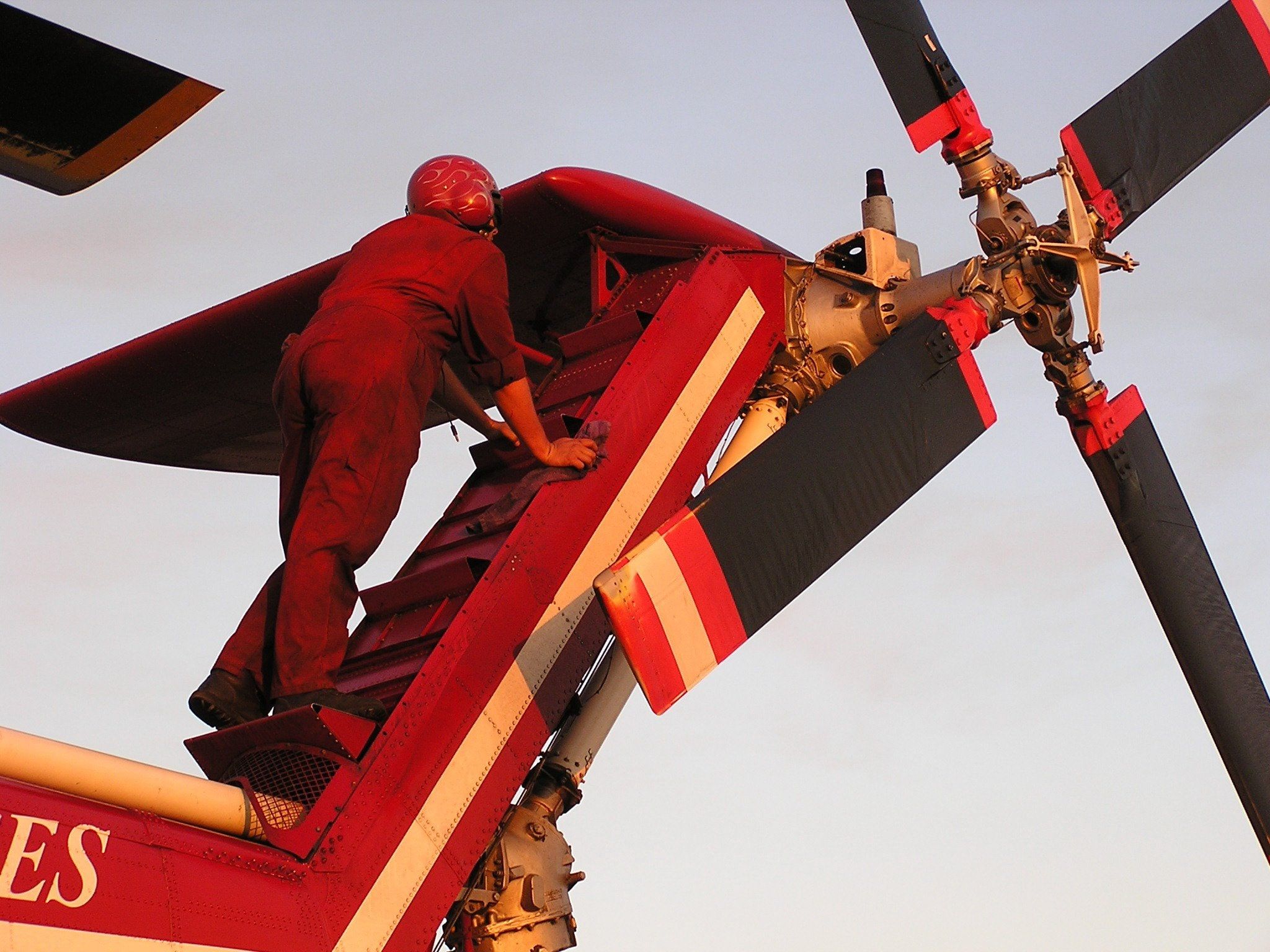 HTS technician working on the rotor head of a Skycrane, blades spread against a pale sky
