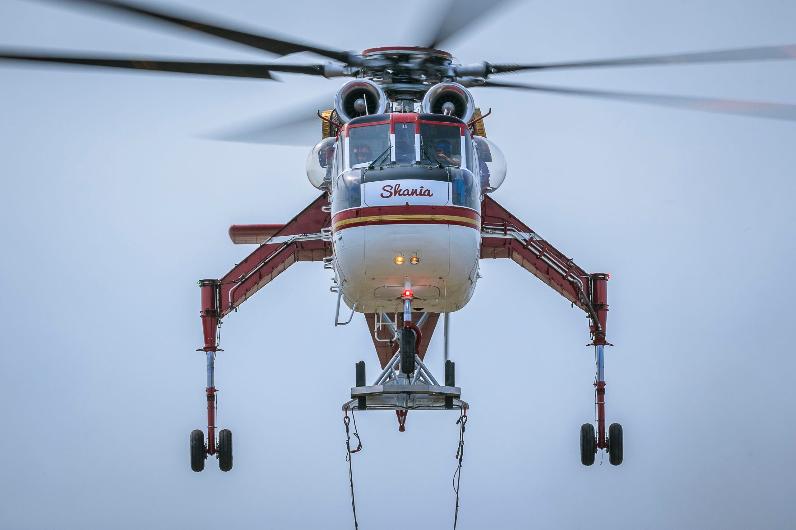 HTS Skycrane hovering head-on, landing gear spread, load frame and slings hanging below