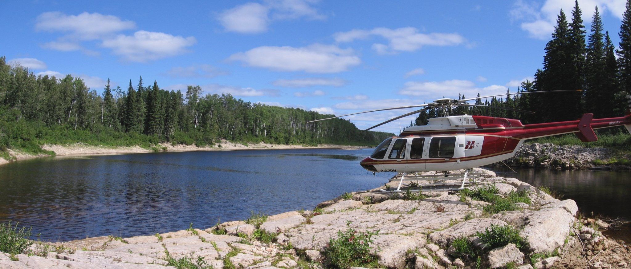 HTS Bell 407 parked on bare rock beside a northern lake