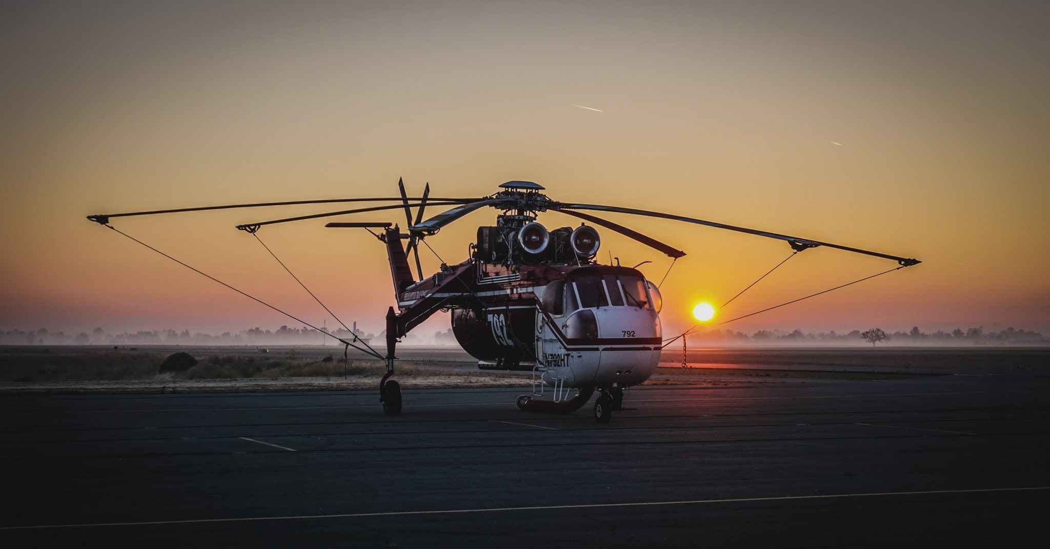 A Skycrane on a ramp at sunrise, its long rotor blades drooping